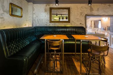 Cozy restaurant booth with dark green tufted seating, wooden tables and stools, and worn rustic walls.