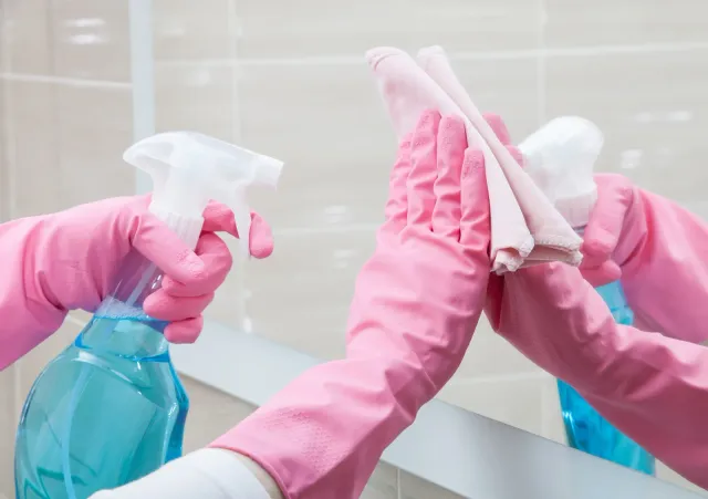 A person wearing pink gloves is cleaning a mirror.