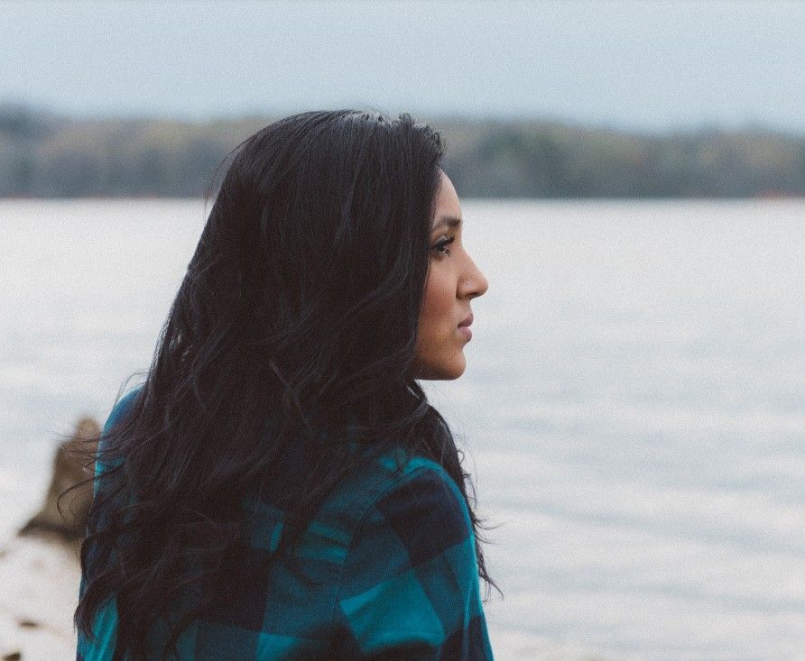 Woman in a teal plaid shirt looking over a calm lake on an overcast day