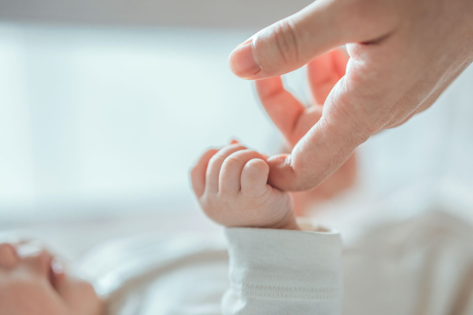 Adult finger holding a newborn’s hand in a white sleeve, close-up