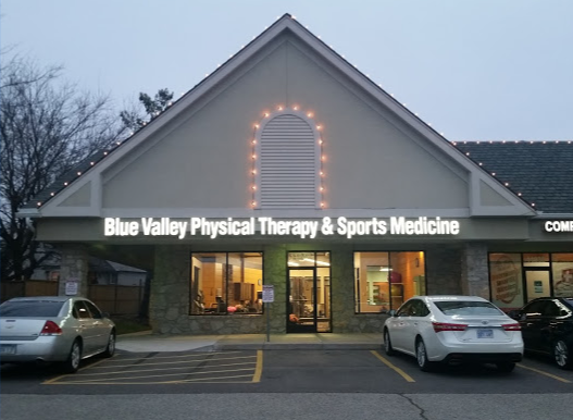 The storefront of Blue Valley Physical Therapy & Sports Medicine with parked cars in front at dusk.
