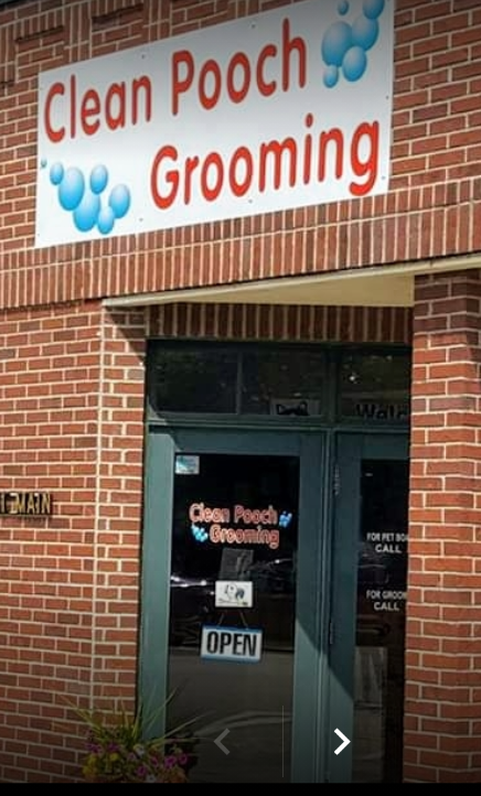 The brick storefront for Clean Pooch Grooming, featuring a sign with blue bubbles and an open door.