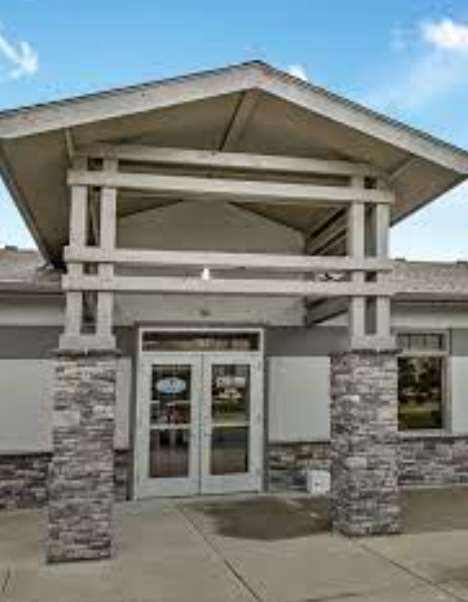 Exterior entrance of a building with a large wooden-trussed gable roof, stone pillars, and glass double doors.