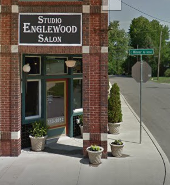 The brick facade of Studio Englewood Salon with potted plants by the entrance and a street sign at a corner.