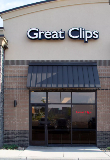 Great Clips storefront with a tan facade, brick accents, and a dark metal awning over the glass entrance doors.