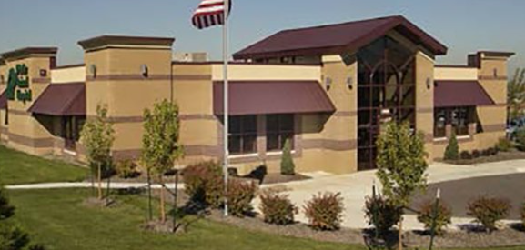 A tan building with a dark maroon roof and matching awnings, with an American flag flying out front.