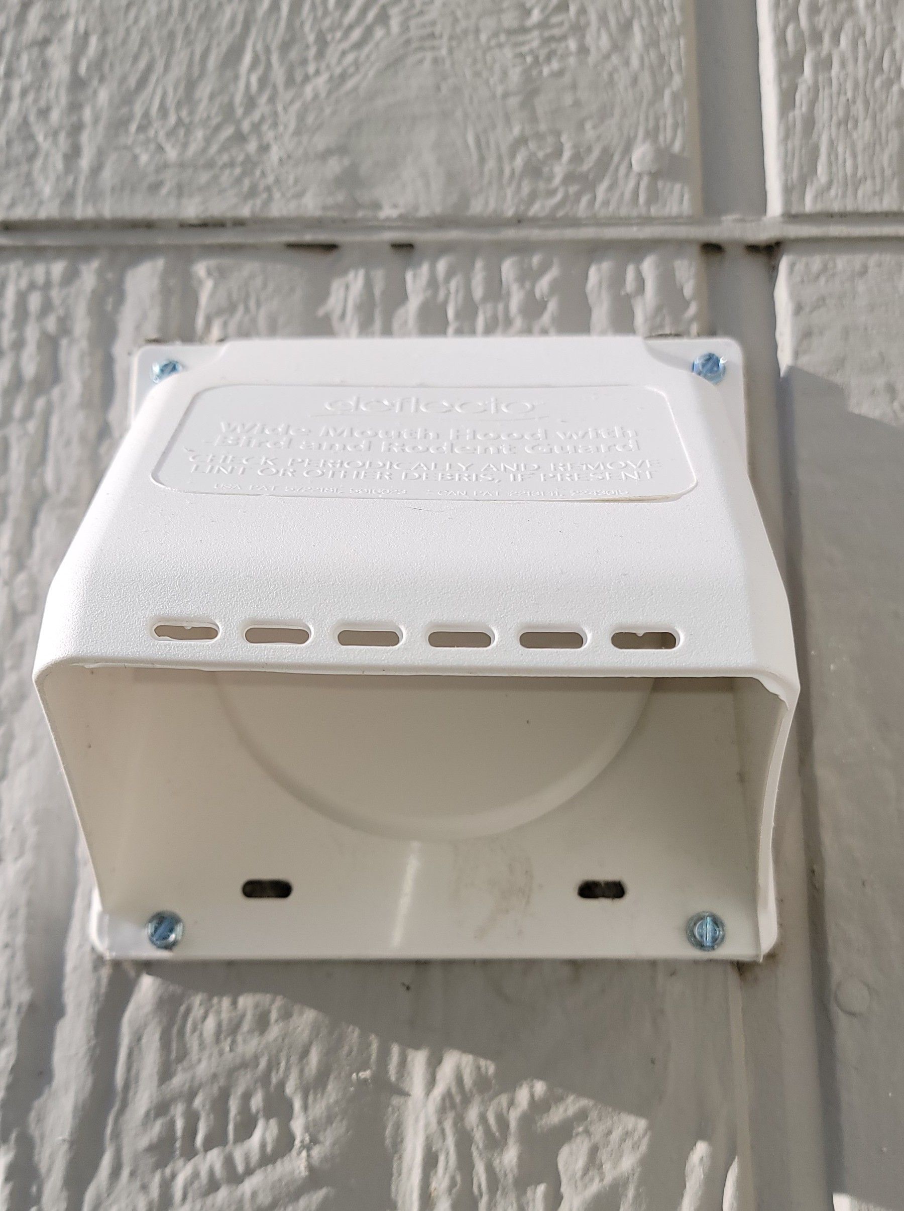 White wall-mounted outdoor siren or speaker box on a textured wall, with vent slots and blue corner screws