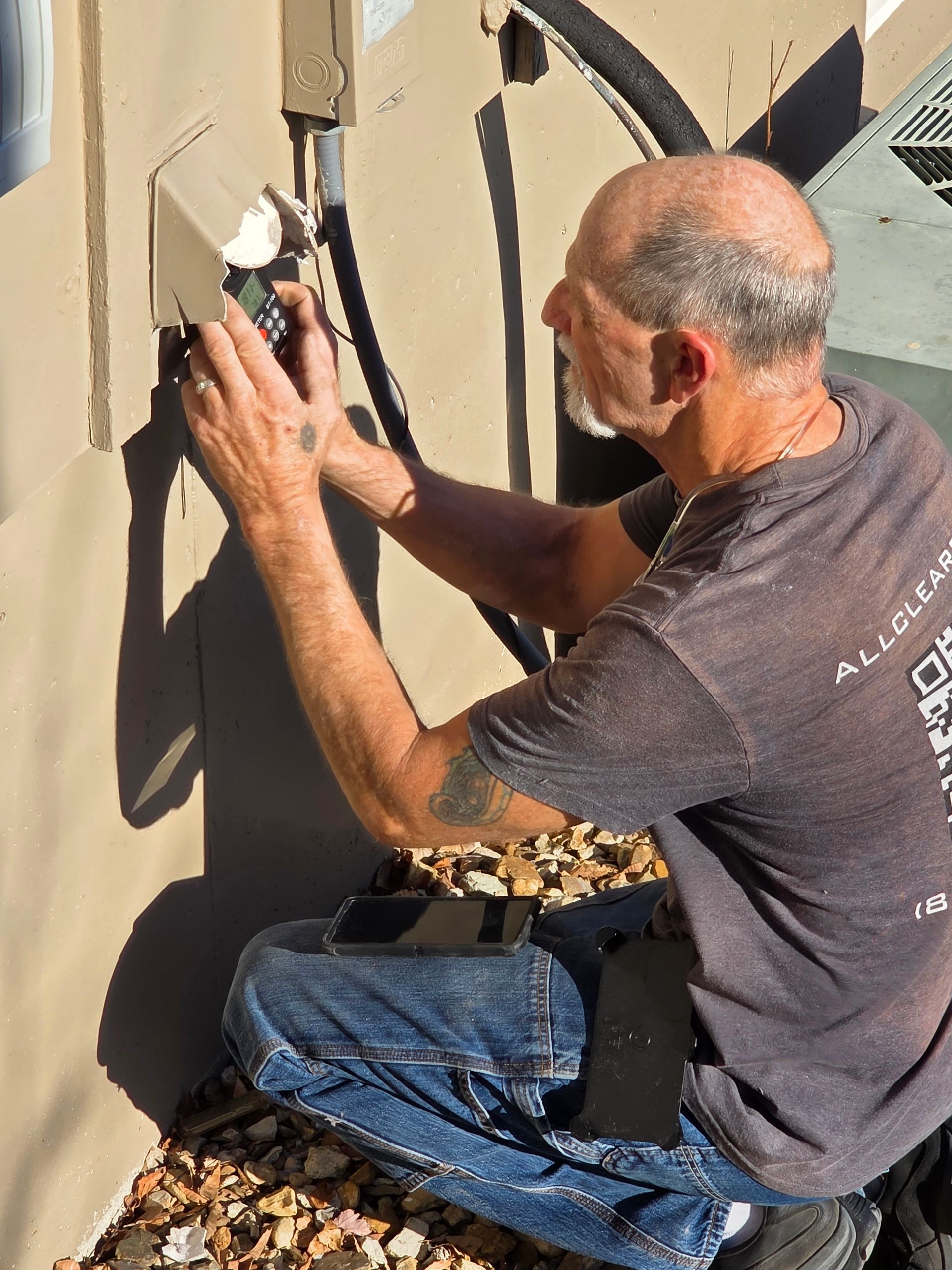 Worker painting an exterior wall with a spray gun, crouched beside a beige building.