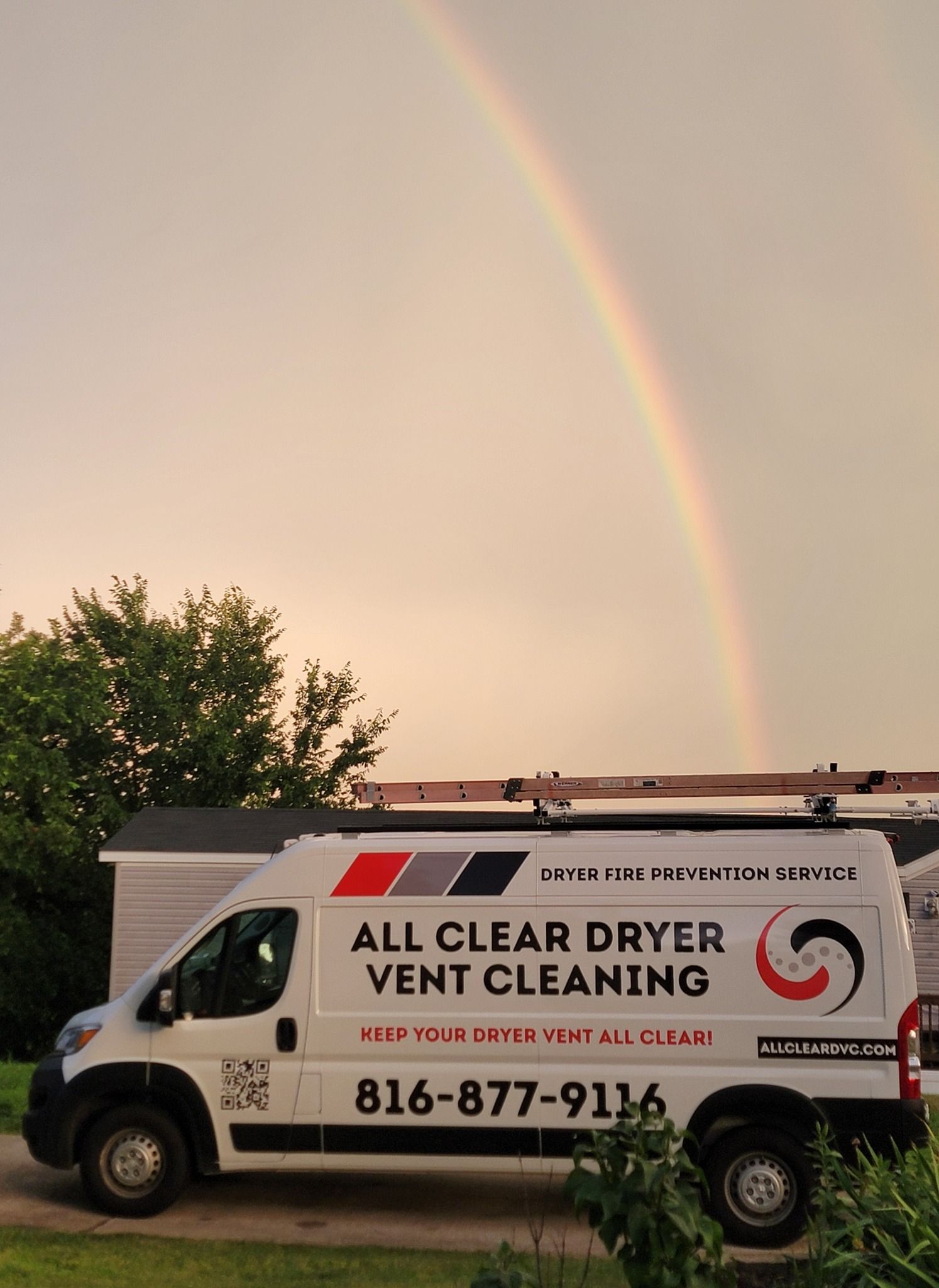 Rainbow over a white vent-cleaning van parked by trees at sunset
