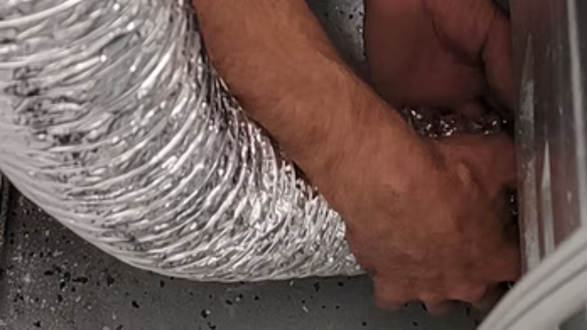 Hands working near a silver insulated duct in a cramped space