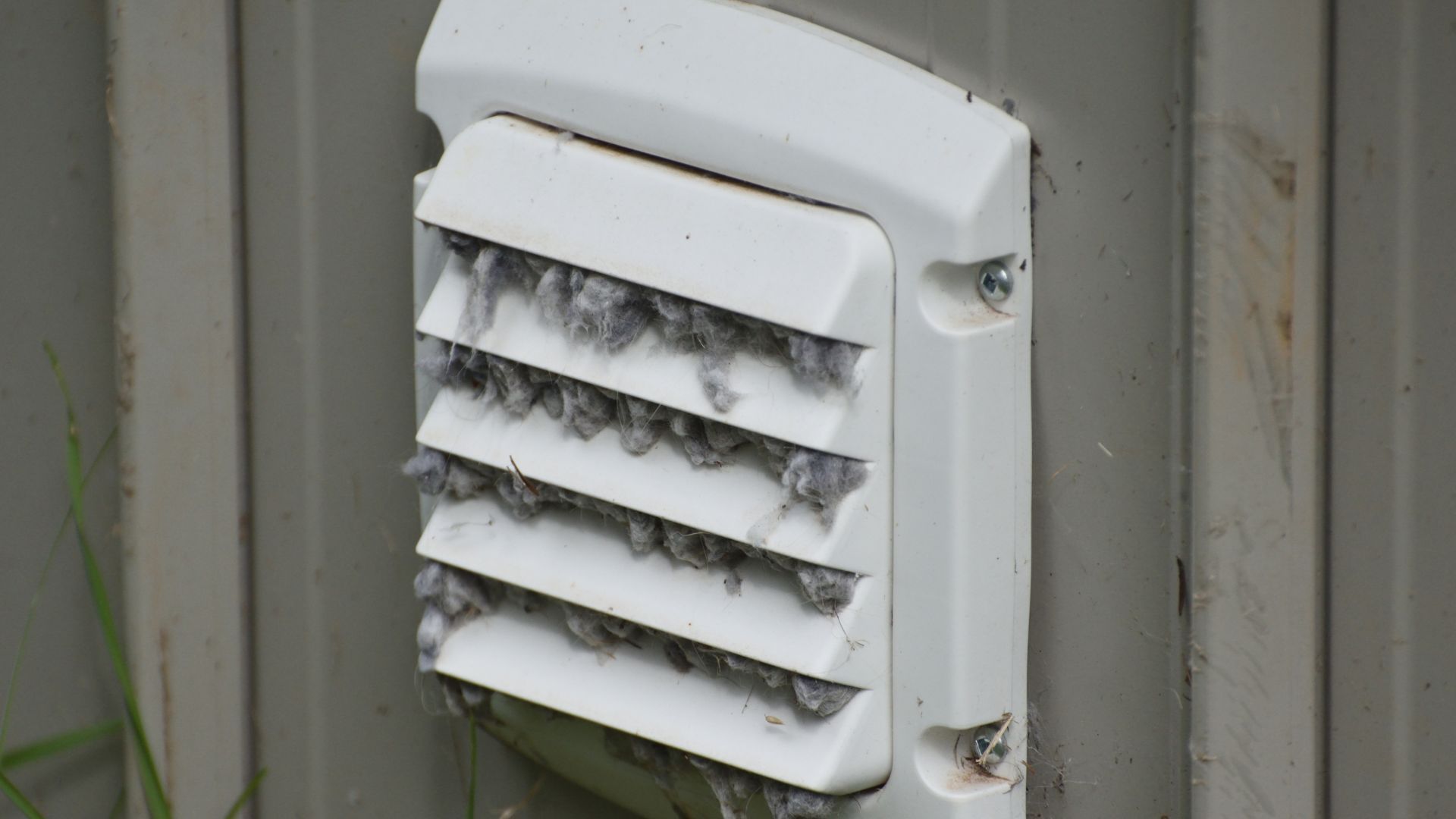 White wall vent with horizontal slats mounted on gray siding outdoors