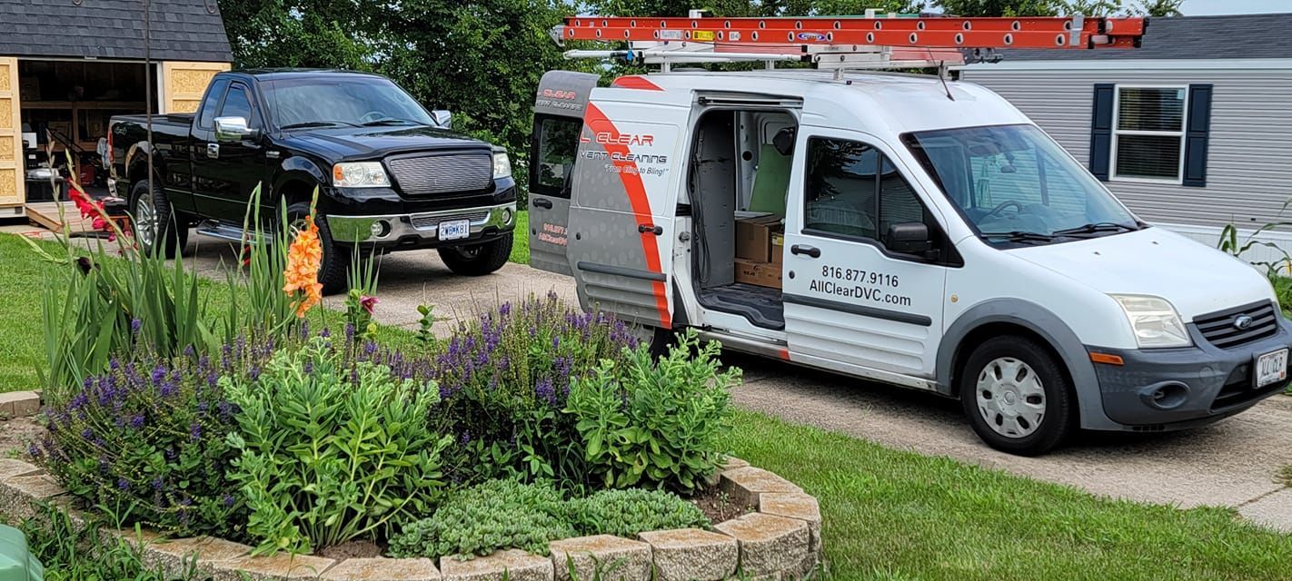 White utility van beside a flower bed, with a black truck parked in the background.