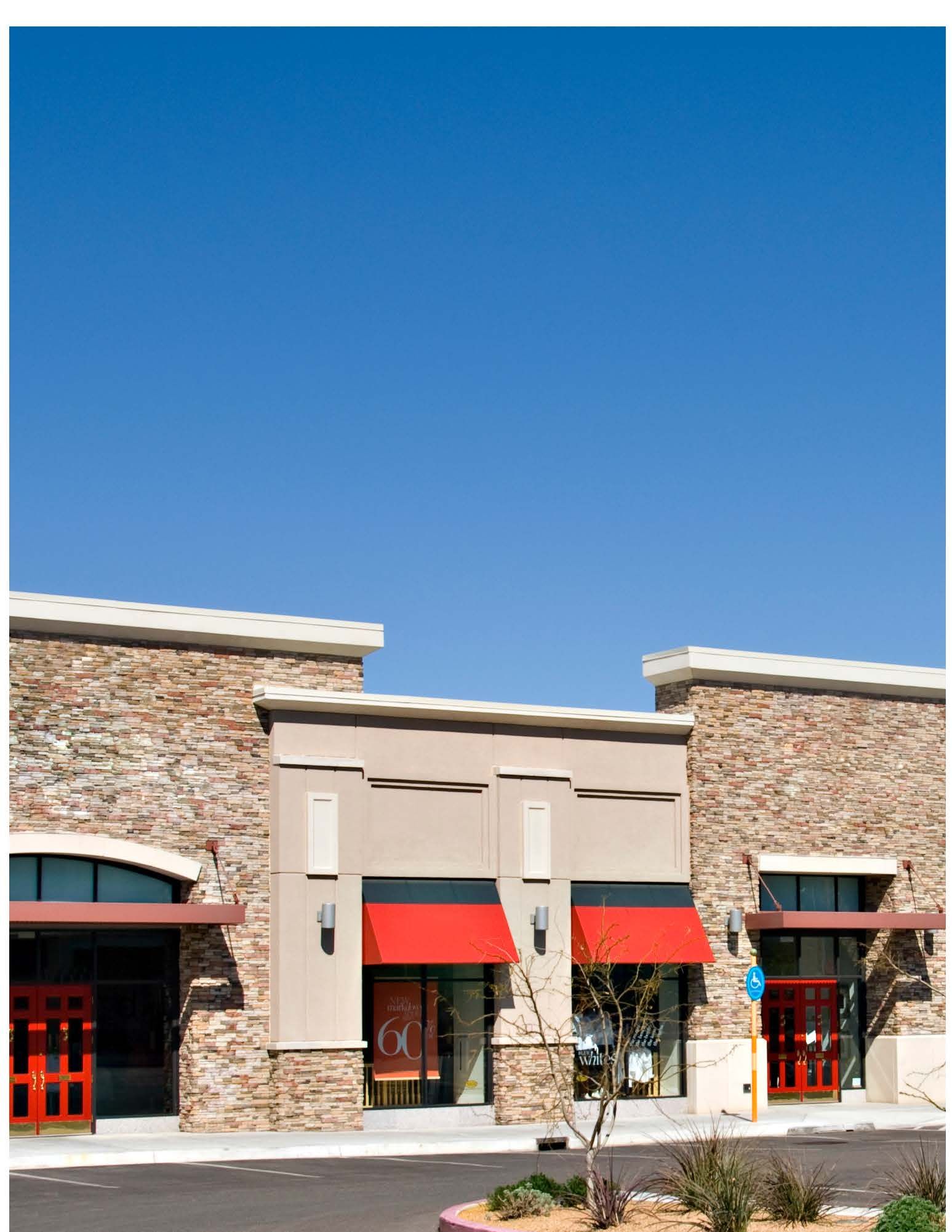 Stone-front storefront with red awnings and red doors under a clear blue sky