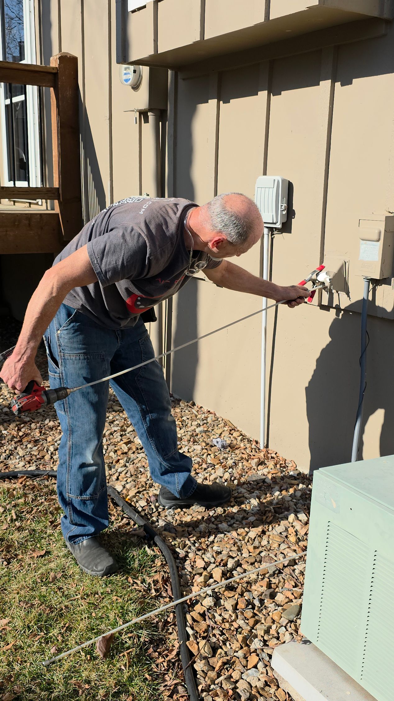 Man using a probe near an outdoor utility box beside a beige building, standing on gravel.