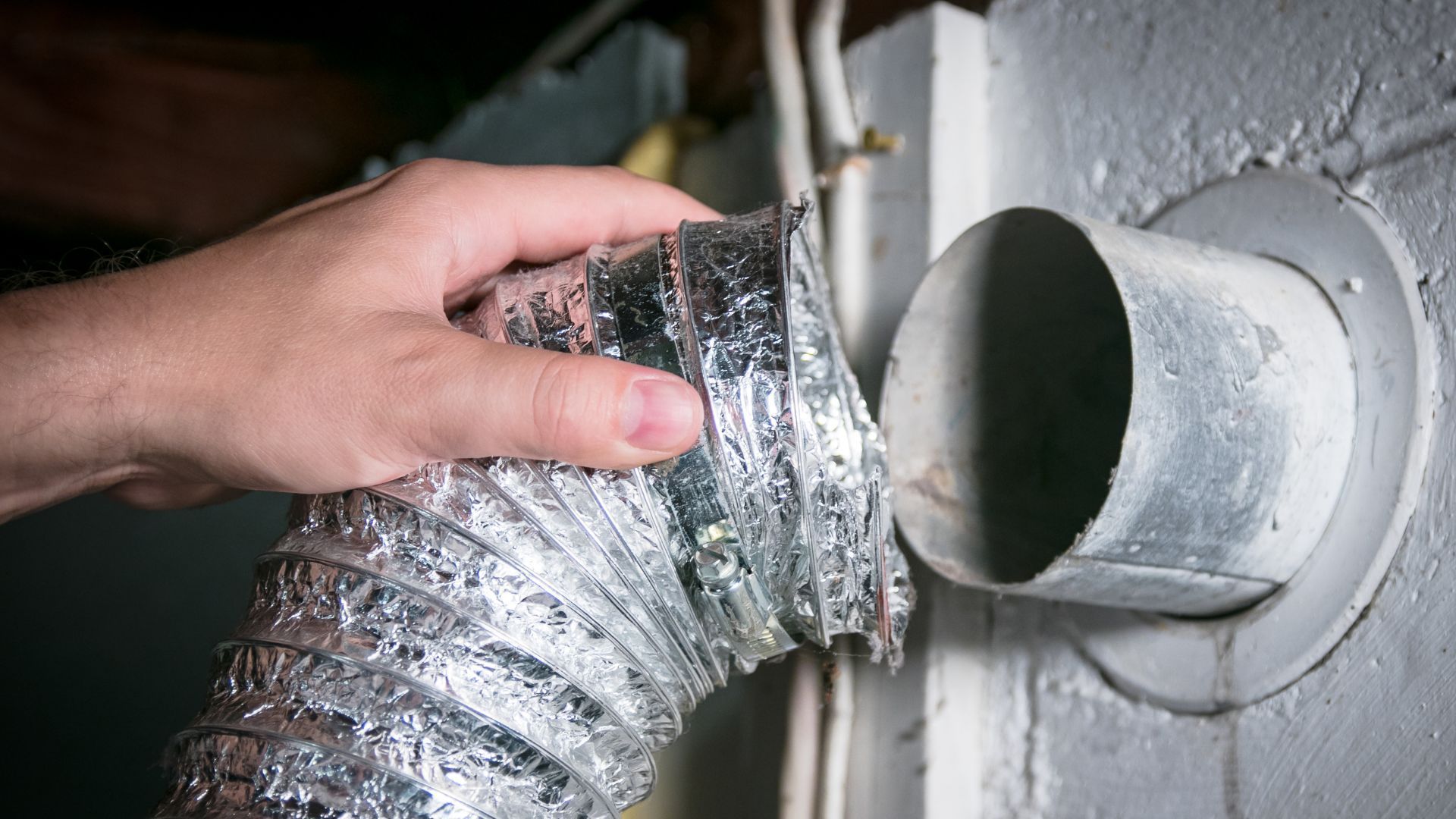 Hand connecting flexible silver duct hose to a white wall vent