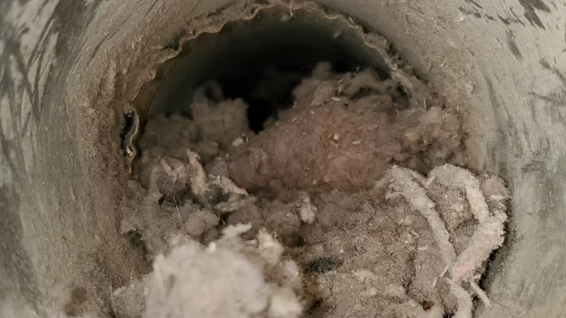 Crumbling circular pipe interior with debris buildup and a dark opening at the center