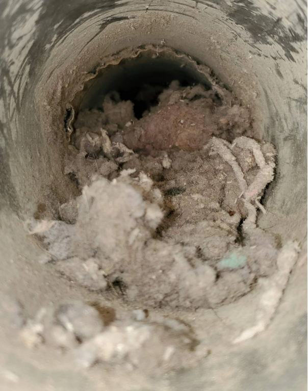 Inside a dusty vent pipe, there is a buildup of lint, dust, and debris.