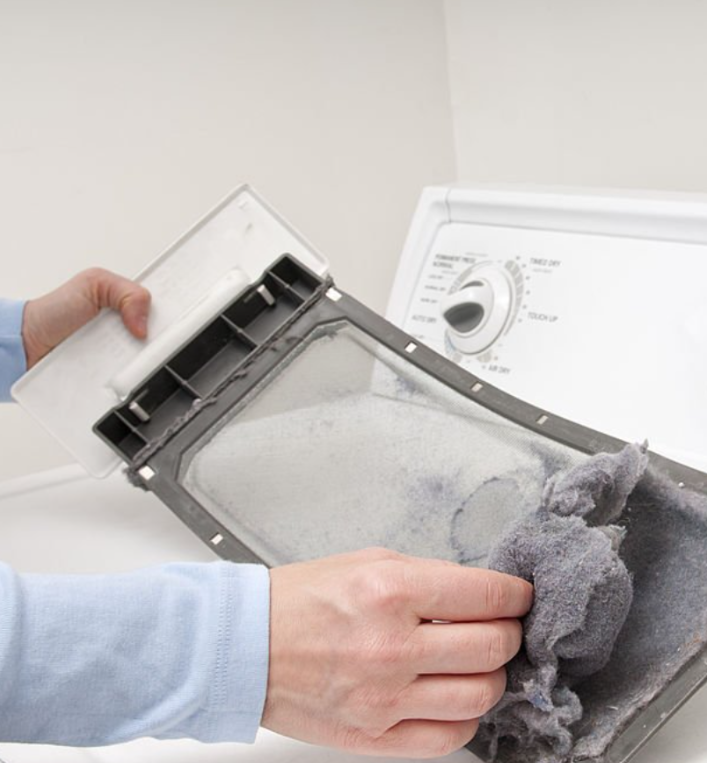 Hands cleaning a lint filter from a washing machine with gray lint buildup