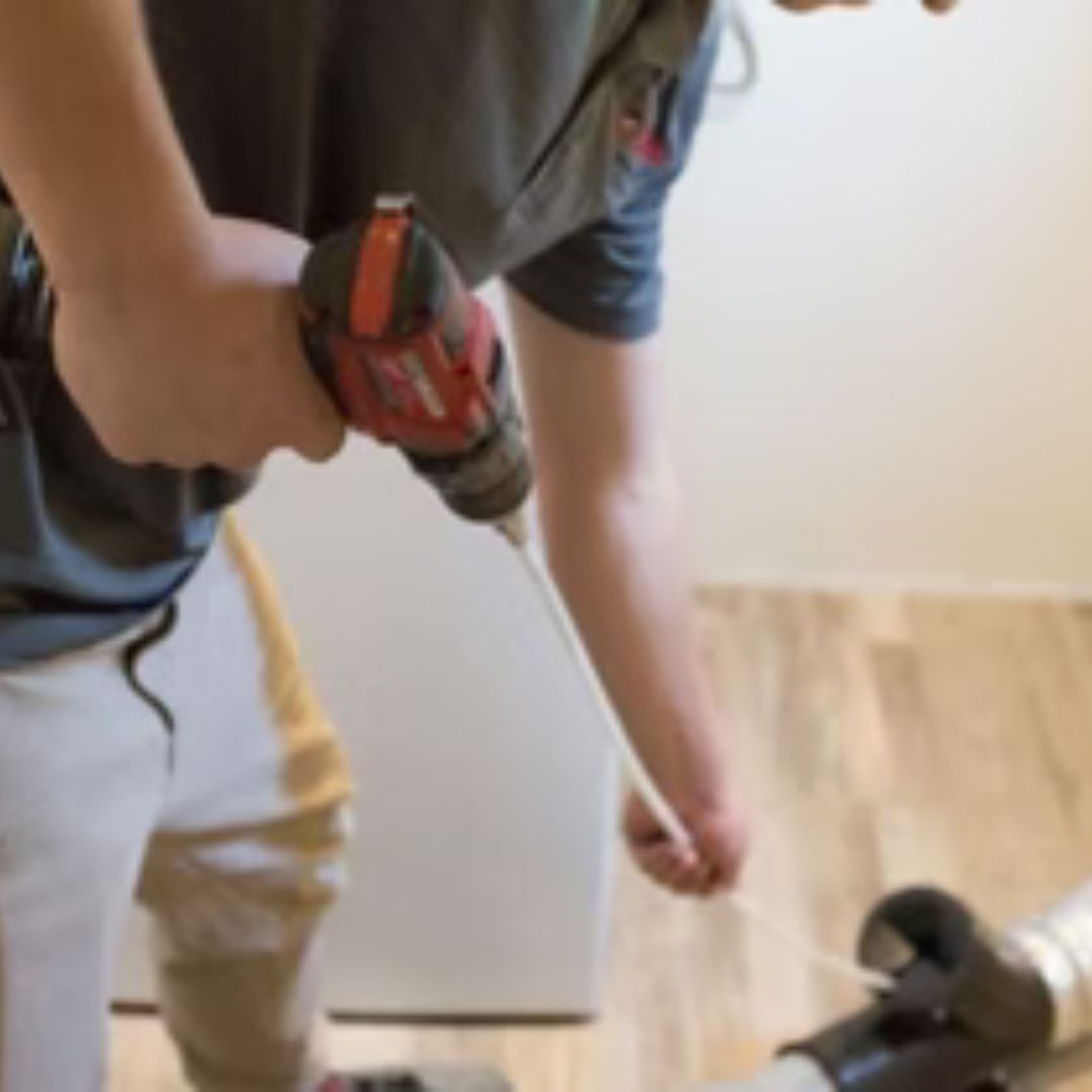 Person using a red drill to work on a light wood floor indoors