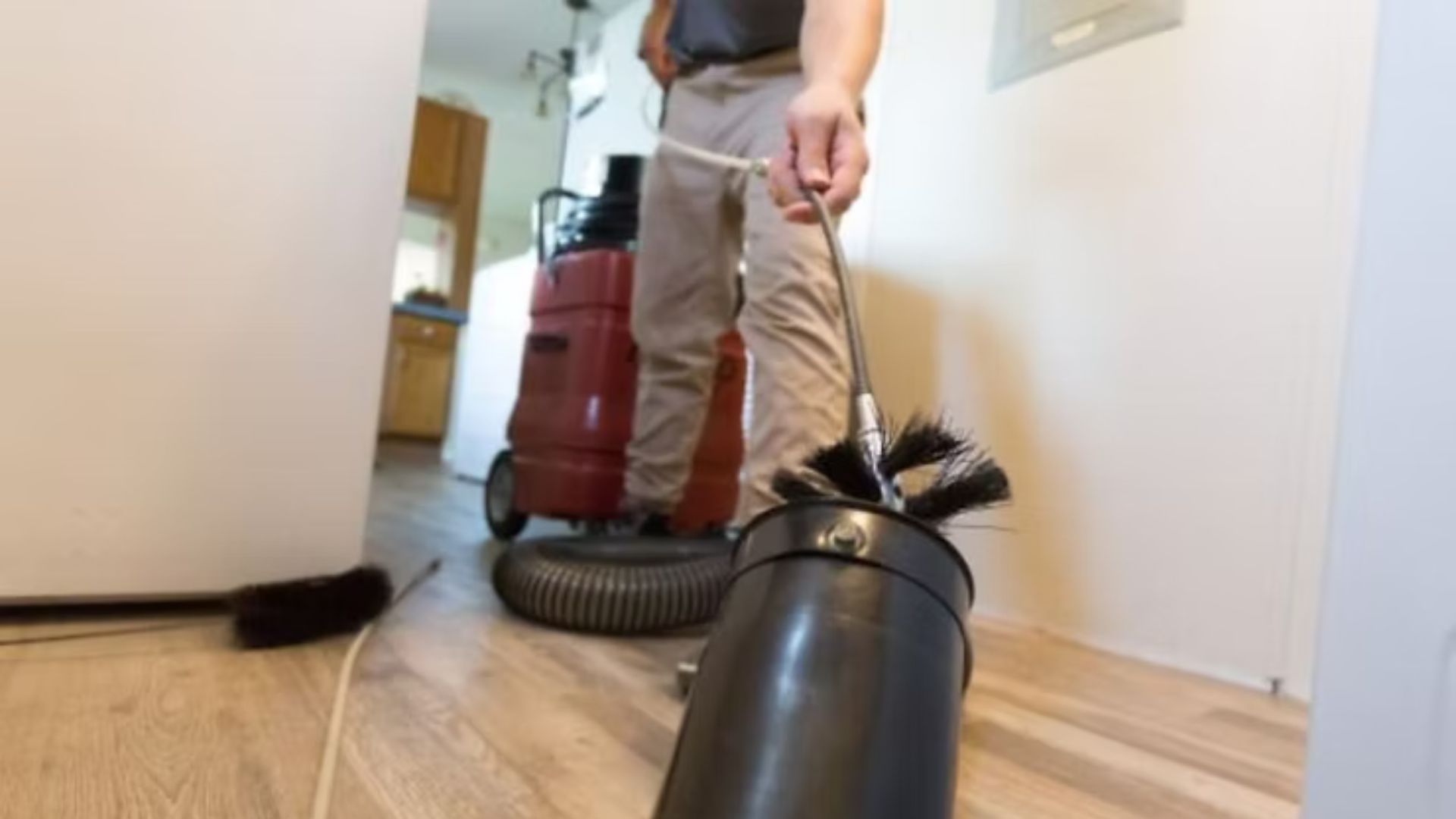 Person vacuuming a hallway floor with a red canister vacuum and black hose