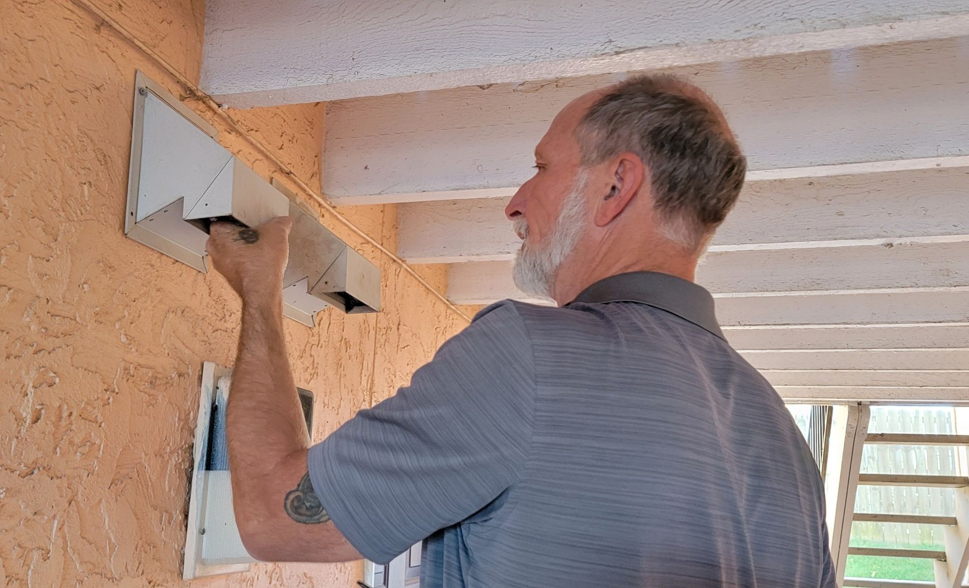 Man applying white trim to a peach-colored wall beneath a porch ceiling