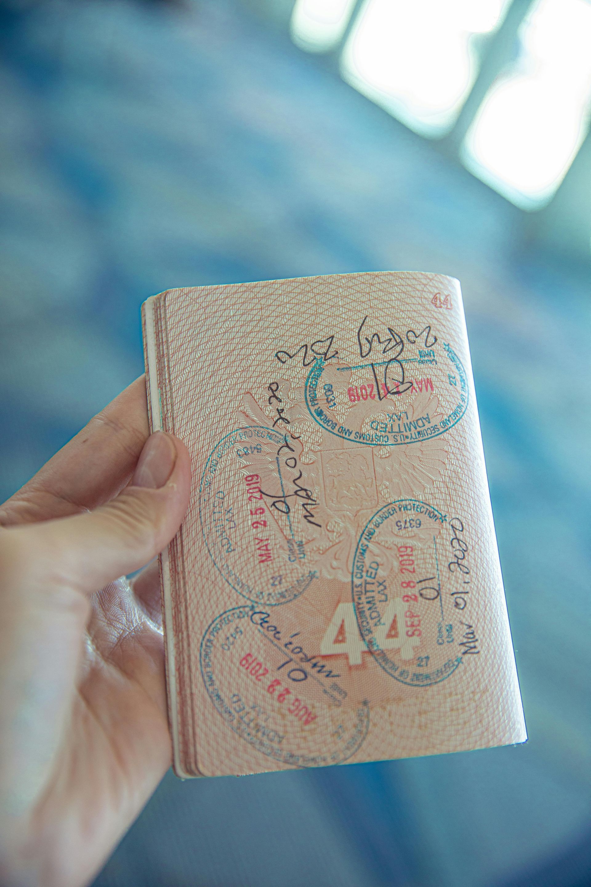 A hand holds a passport page with multiple travel stamps and a prominent