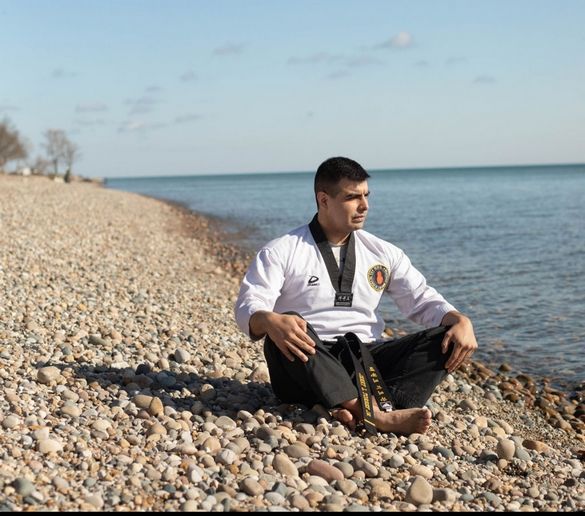 A man is sitting on a rocky beach near the water