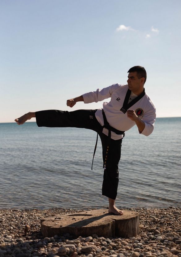 A man is practicing karate on the beach near the water