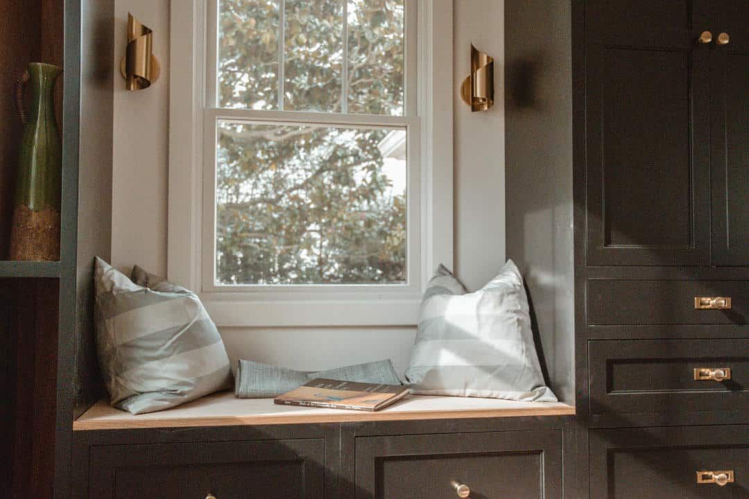 There is a window seat with pillows and a book on it.