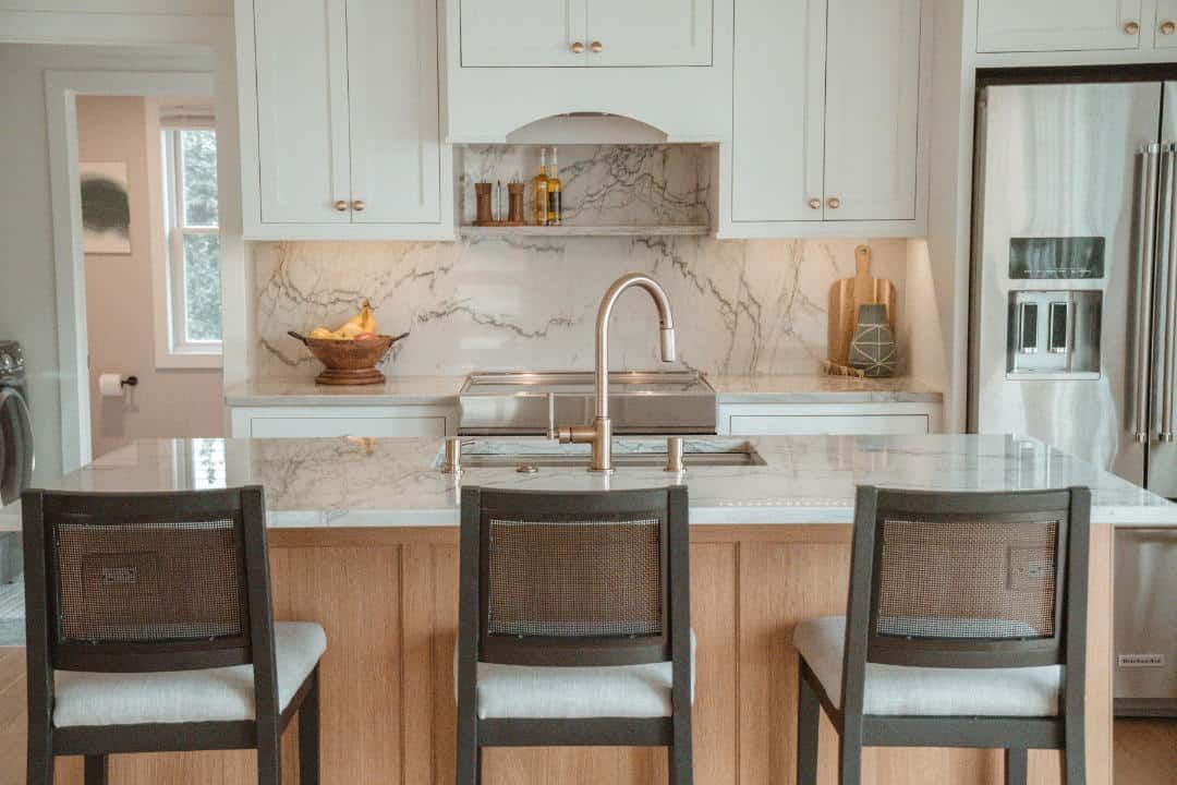A kitchen with a sink , stove , refrigerator and chairs.