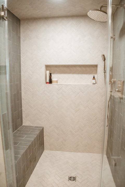 A walk in shower with a bench and a shower head.