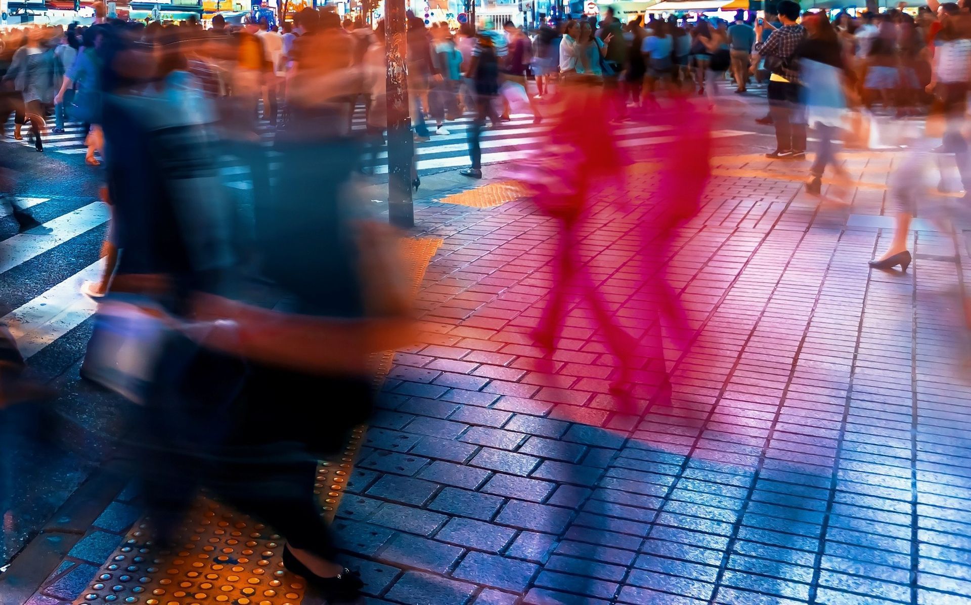 Blurred pedestrians crossing a wet cobblestone street, with a bright pink figure in the center