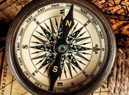 Vintage compass on a rustic wooden surface, showing north with a beige-and-black dial.