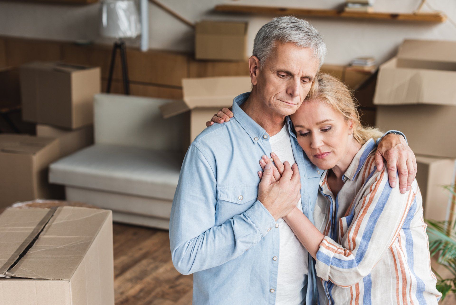 A man and a woman are hugging each other in a living room filled with cardboard boxes.