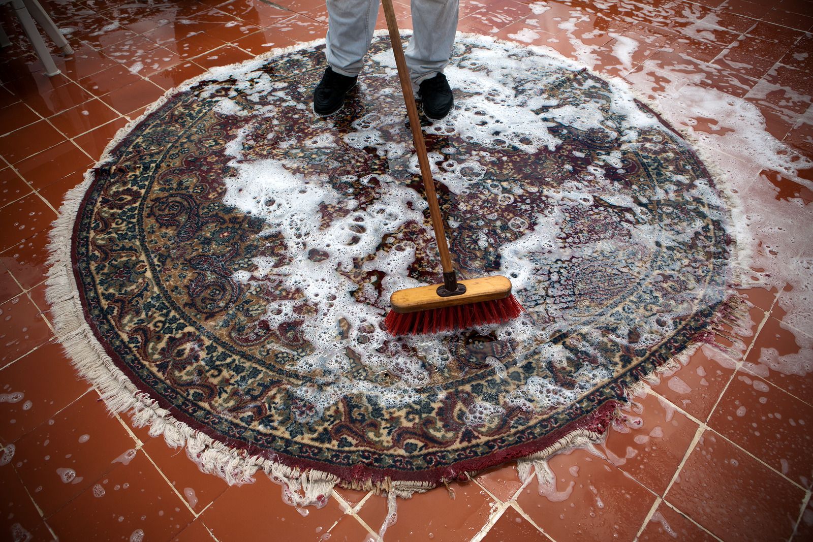 A person is cleaning a rug with a broom.