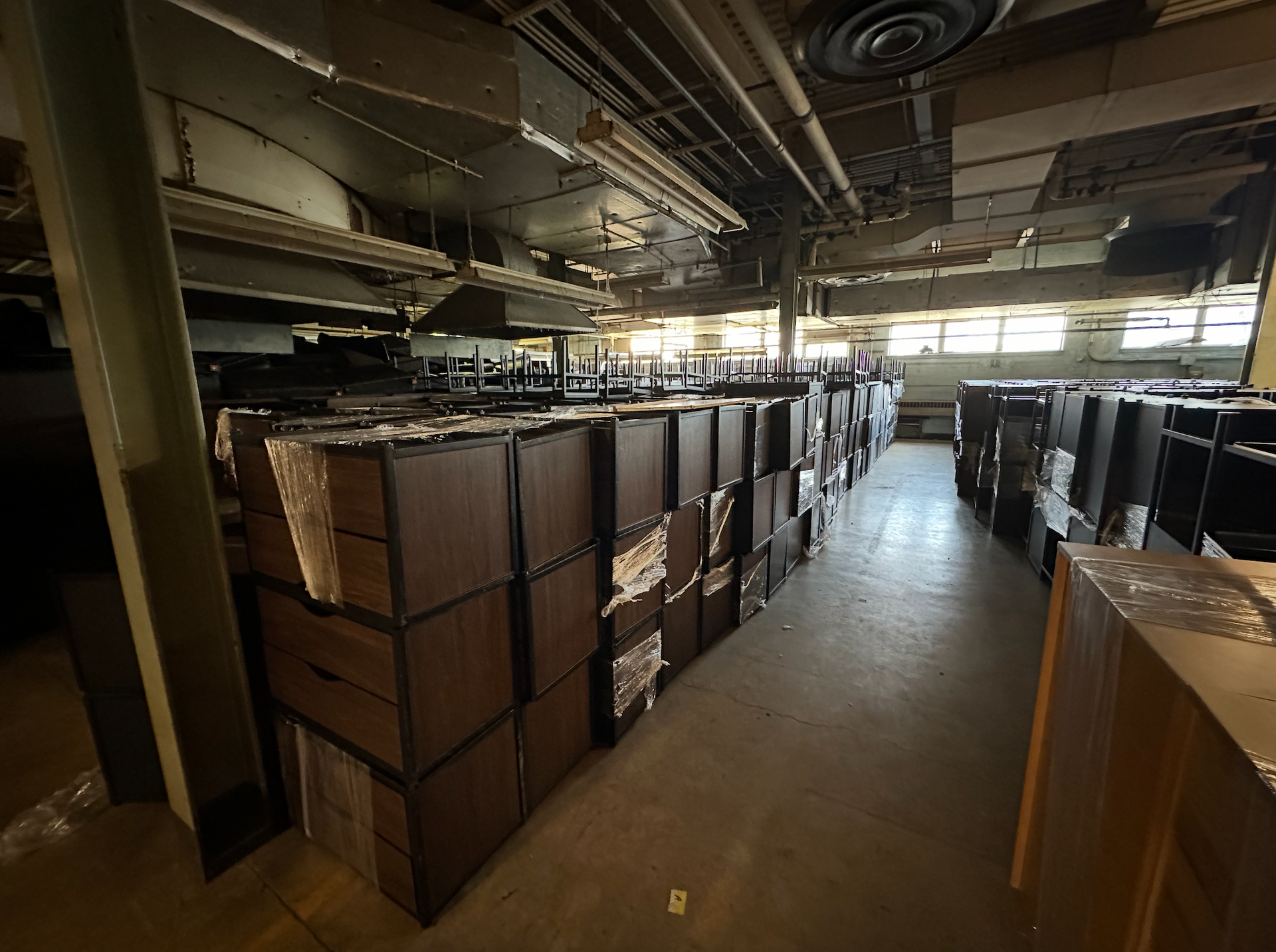 Rows of stacked, dark brown cabinet units in a dimly lit, industrial warehouse storage space.