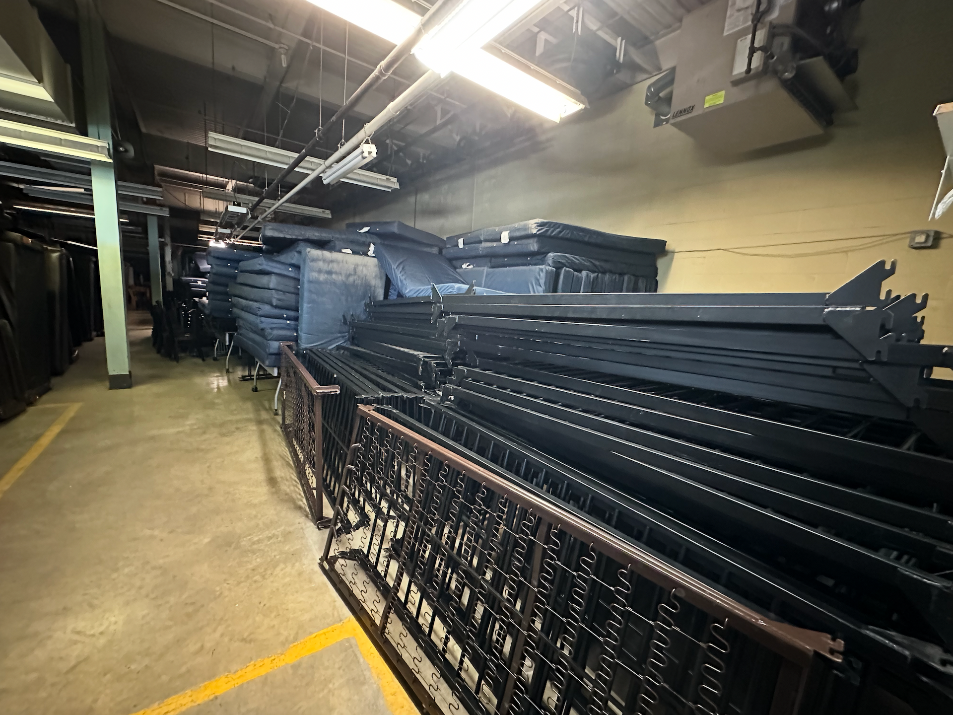A storage area filled with stacks of dark metal bed frames and support structures on a concrete floor.