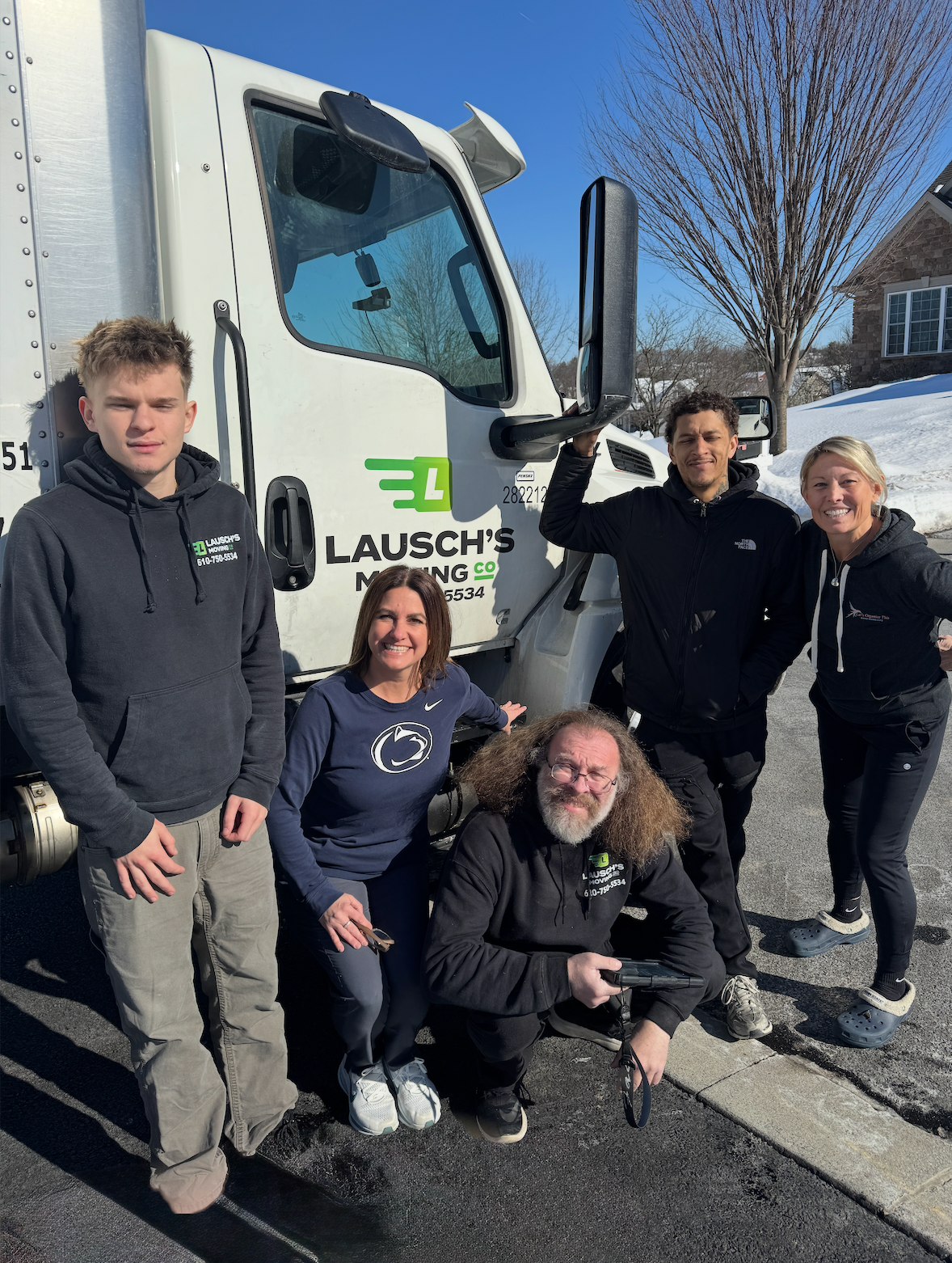 Five people stand and crouch in front of a white delivery truck branded
