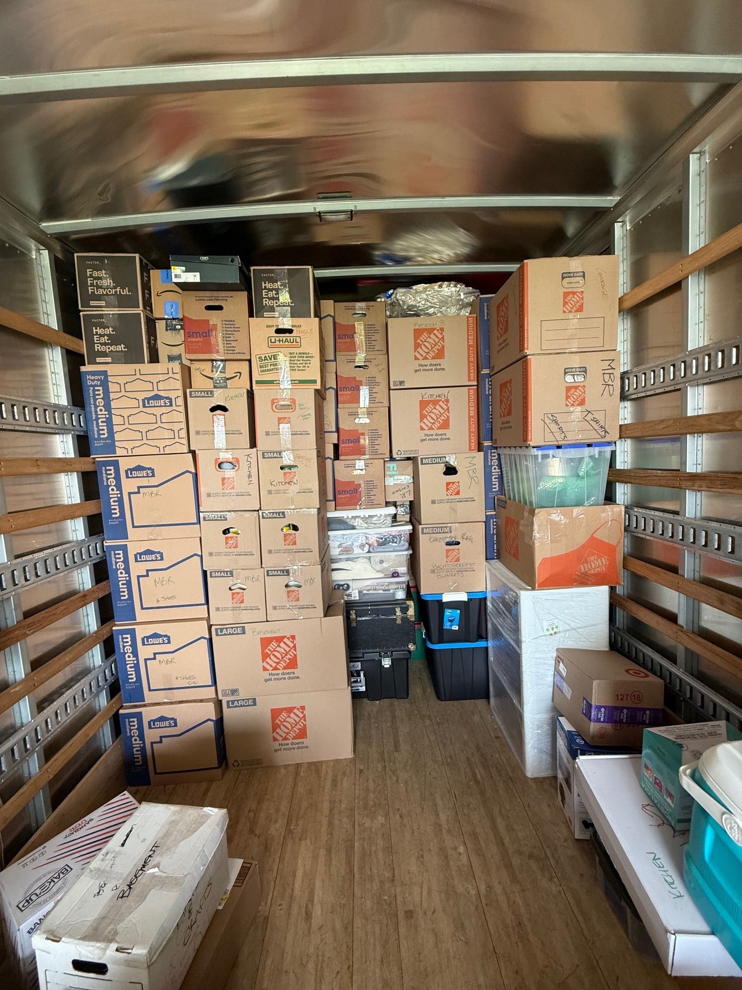 A moving truck interior packed with stacked cardboard boxes, plastic bins, and furniture.