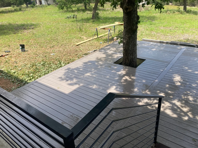 Shaded wooden deck with a tree in the center overlooking a grassy park area