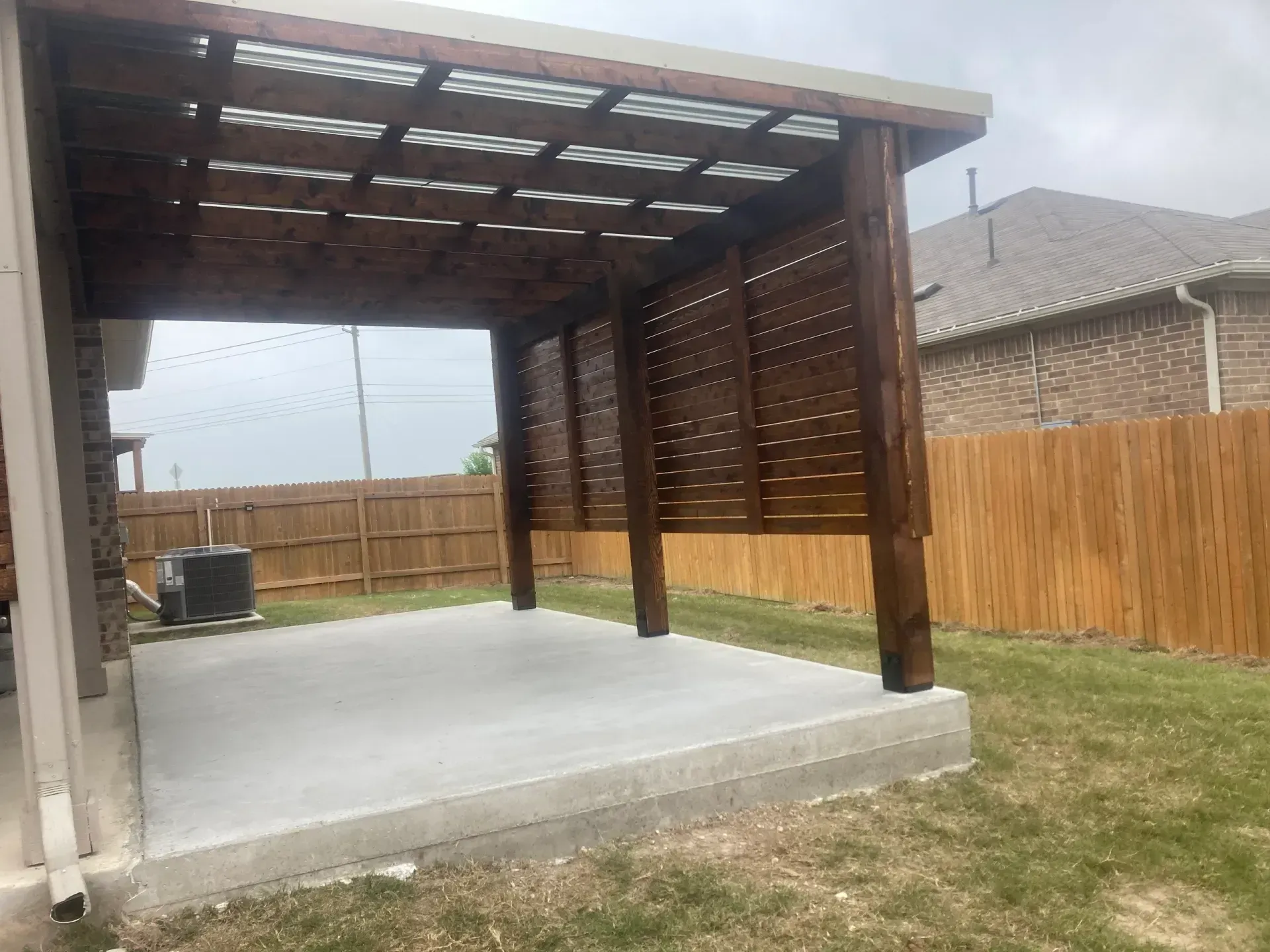 Wooden backyard patio cover over a concrete slab beside a fence and grass yard