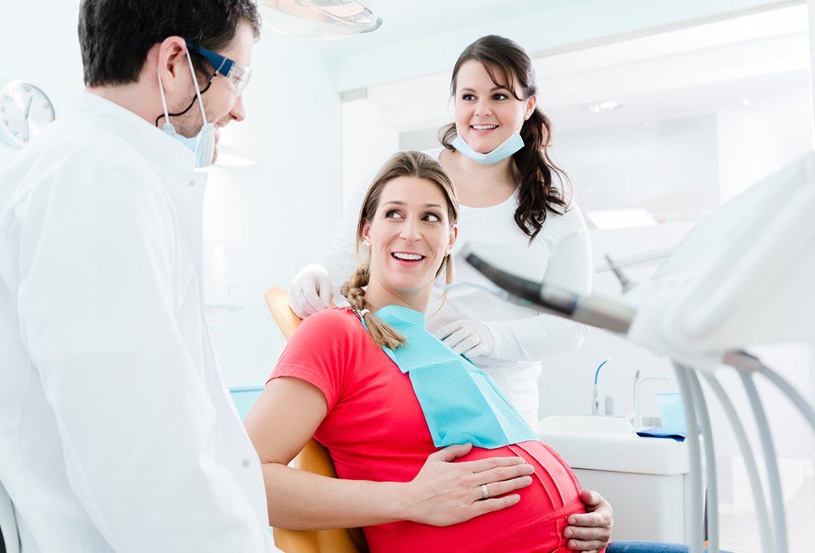 Pregnant patient smiling in a dental clinic while dentist and assistant stand nearby