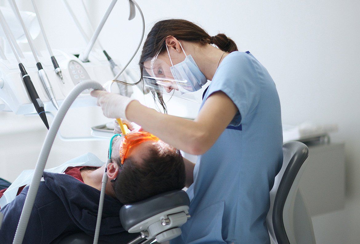 Dentist treating a patient in a bright clinic, using tools and a face shield.
