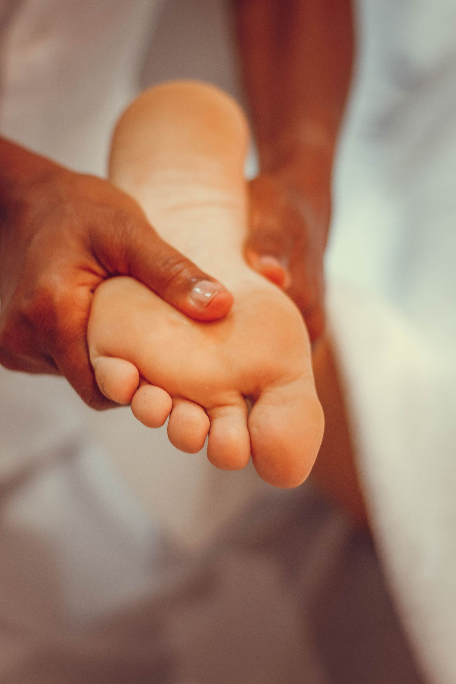 Close-up of a hand holding the sole of a baby’s foot against a soft, blurred background