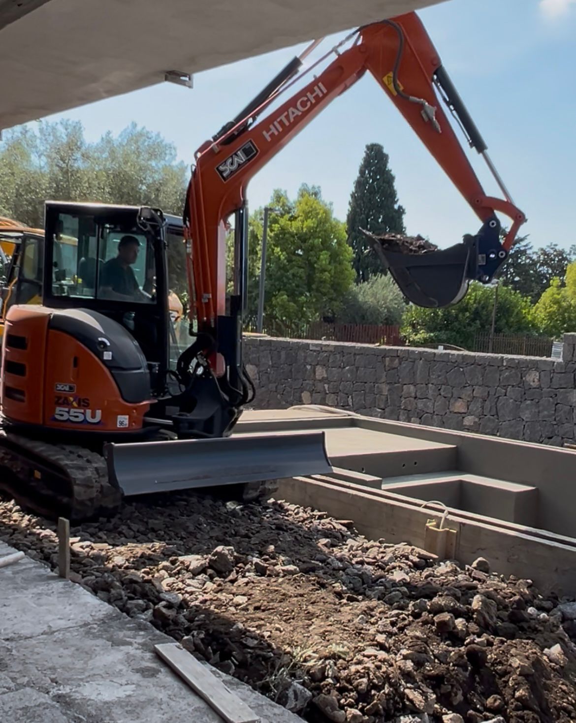 Escavatore Bobcat su un rimorchio rosso, caricato su un camion con pianale su una strada asfaltata.