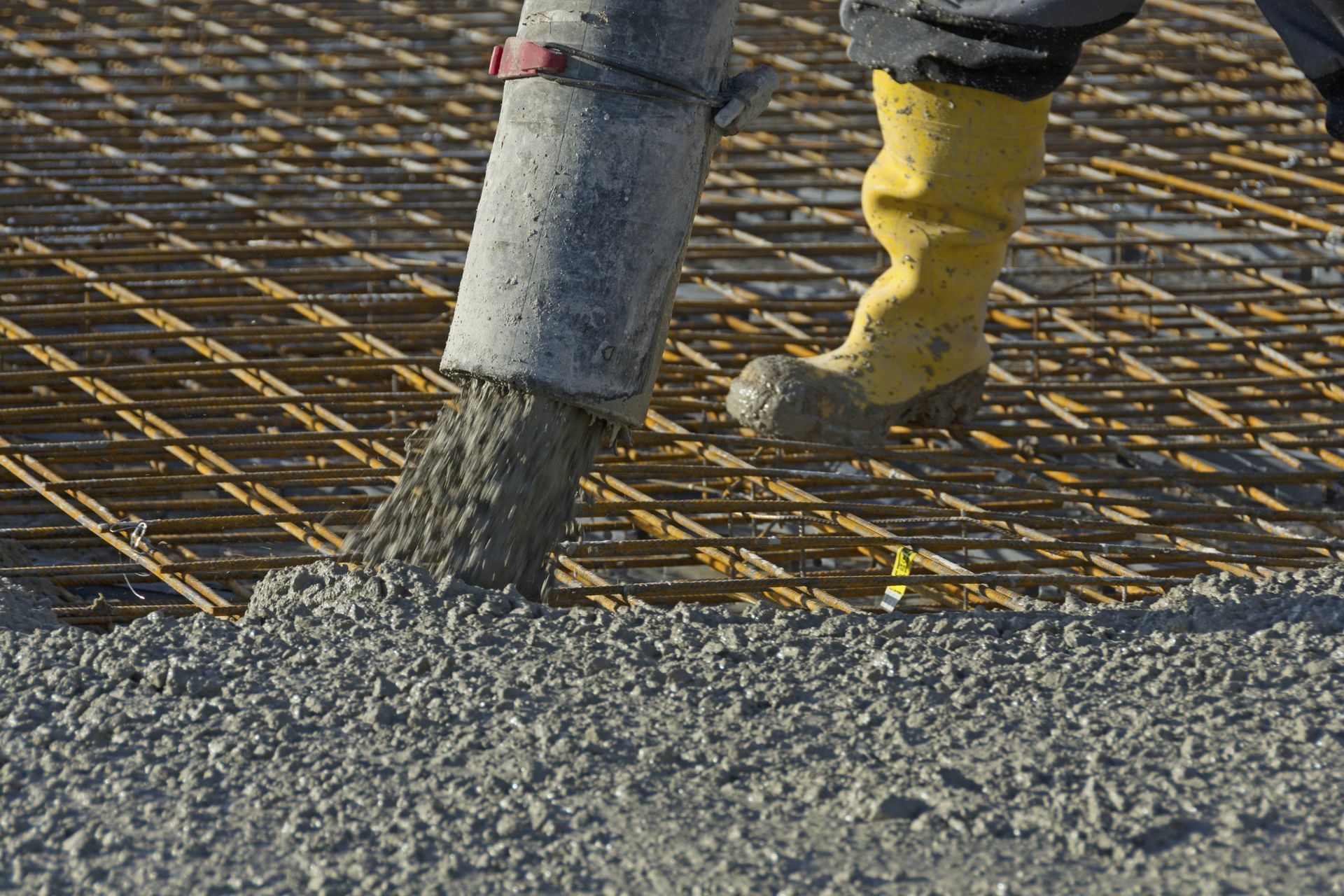 Beton wird auf ein Bewehrungsgitter gegossen; Arbeiter in gelben Stiefeln.