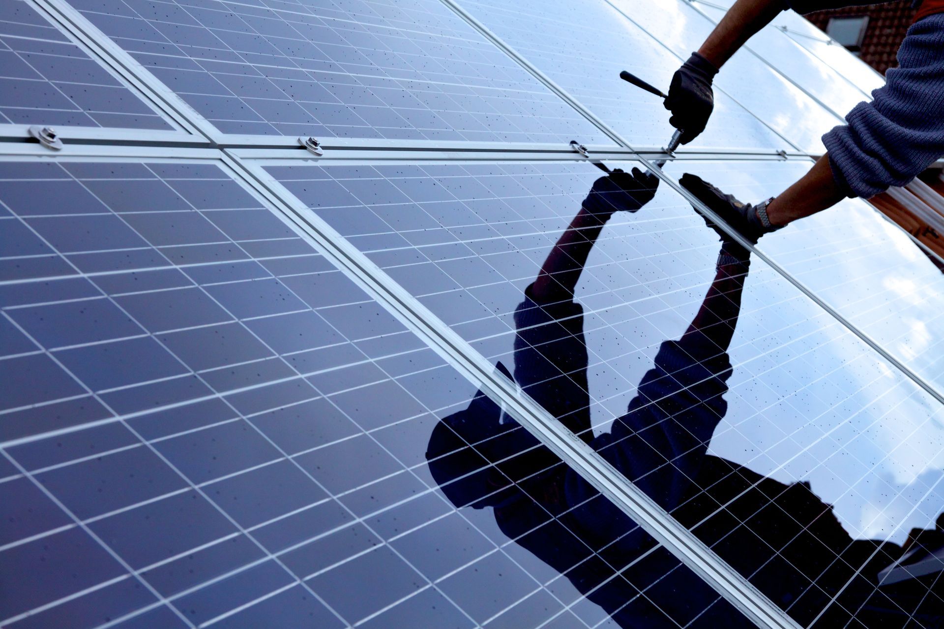 Person installiert Solarmodule auf einem Dach, Spiegelung sichtbar.