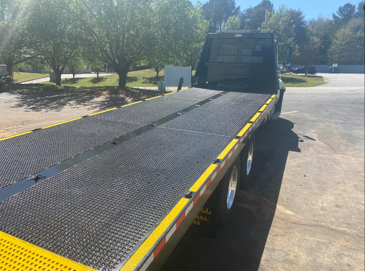A flatbed tow truck is parked in a parking lot
