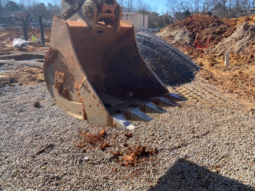 A large excavator bucket is sitting on top of a gravel road.