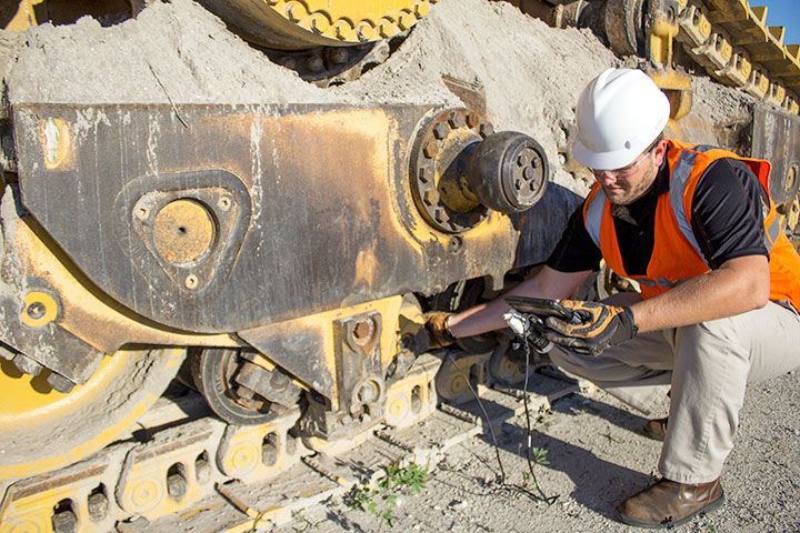 Man in safety vest and hard hat inspects bulldozer track.